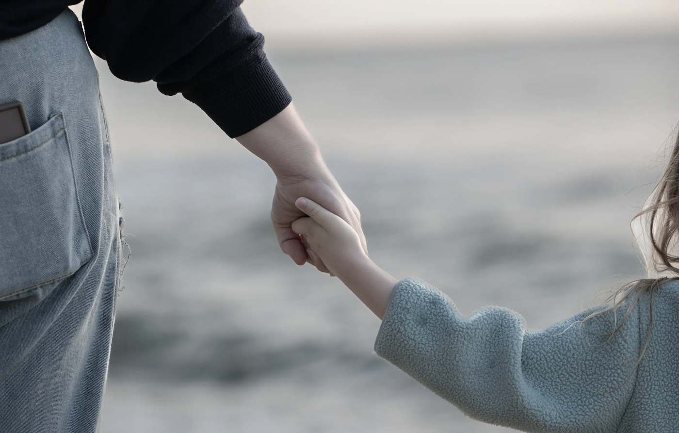 An adult and a child holding hands by the sea